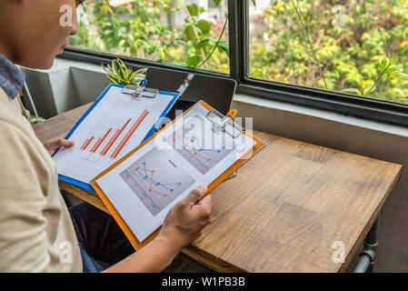 Asian freelancer holding and analyzing statistic documents at rustic workplace Stock Photo