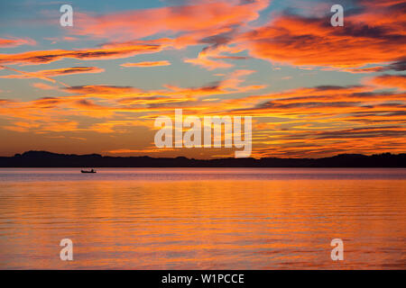 Anglers with small motor boat in the last evening light at sunset on Lake Chiemsee, dramatic color and clouds mood Stock Photo