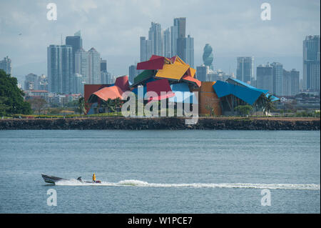 A power boat passes in front of the Panama City skyline featuring the colorful Biomuseo museum designed by Frank Gehry, Panama City, Panama, Central A Stock Photo