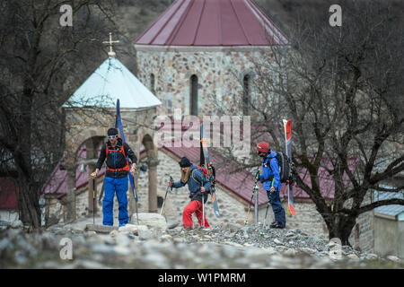 Three young skiers walking past a church in a village, Gudauri, Mtskheta-Mtianeti, Georgia Stock Photo