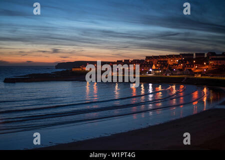 City lights reflect in the water of the Atlantic Ocean at Kilkee Bay under a pink sky during sunset, Kilkee, County Clare, Ireland, Europe Stock Photo