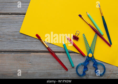 Childrens art and craft composition. Art supplies and yellow paper on a desk Stock Photo