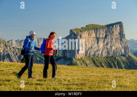 A man and a woman walking on meadow with Mont Aiguille in the background, from the Tête Chevalier, Vercors, Dauphine, Dauphine, Isère, France Stock Photo