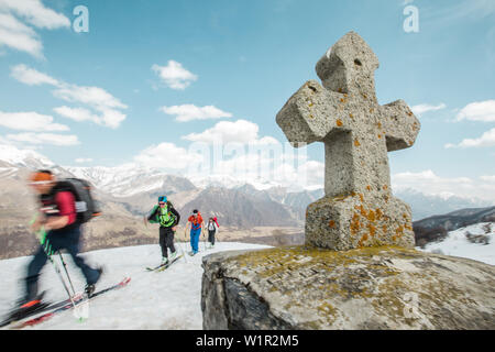 A group of skiers walking past a stone cross in the mountains, Gudauri, Mtskheta-Mtianeti, Georgia Stock Photo