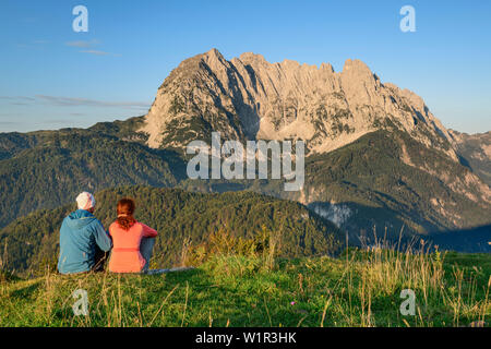 A man and a woman sitting on meadow and views of the Wilder Kaiser mountain, in the dawn, from behind Wilder Kaiser, Kaiser mountains, Tyrol, Austria Stock Photo