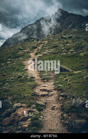 Long distance hiking trail with foggy peaks in the background, E5,Alpenüberquerung,5th stage, Braunschweiger Hütte,Ötztal, Rettenbachferner, Tiefenbac Stock Photo