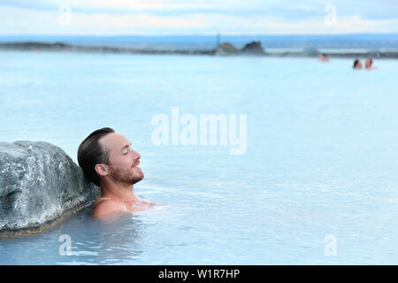 Geothermal spa. Man relaxing in hot spring pool on Iceland. Young man enjoying bathing relaxed in a blue water lagoon Icelandic tourist attraction. Stock Photo