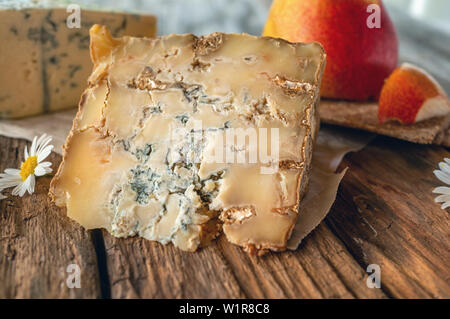 A slice of blue aged Stilton cheese on a wooden table. Cheese is served with a beautiful ripe pear. The quality of farmers ' agricultural products. De Stock Photo