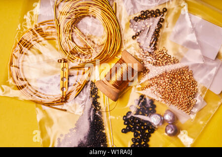 Embroidery products and tools. Coil of metal thread, Japanese beads and sequins with pin and needles on yellow background Stock Photo