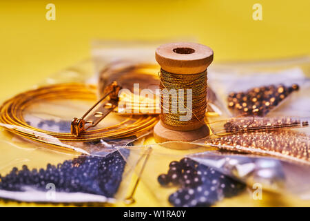 Embroidery products and tools. Coil of metal thread, Japanese beads and sequins with pin and needles on yellow background Stock Photo