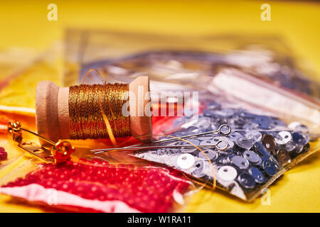 Embroidery products and tools. Coil of metal thread, Japanese beads and sequins with pin and needles on yellow background Stock Photo