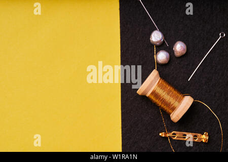 Embroidery products and tools. Coil metal threads, pearls and a pin with the needle on the black felt. Stock Photo