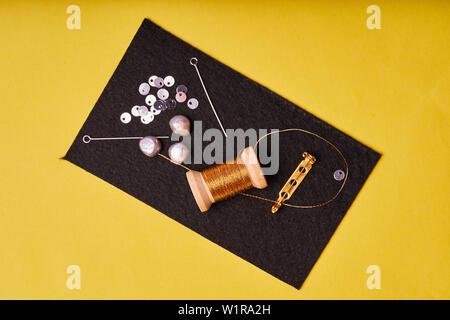 Embroidery products and tools. Coil metal threads, pearls and a pin with the needle on the black felt. Stock Photo