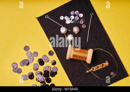 Embroidery products and tools. Coil metal threads, pearls and a pin with the needle on the black felt. Stock Photo