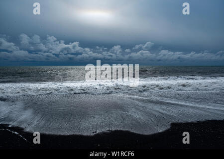 The rocky black sand beach of Reynisfjara on the southeastern coast of Iceland with low lying clouds in the distance Stock Photo