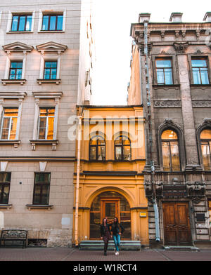 Two attractive girls stand near beautiful old European buildings on a sunny day in St. Petersburg. yellow bright building. Stock Photo