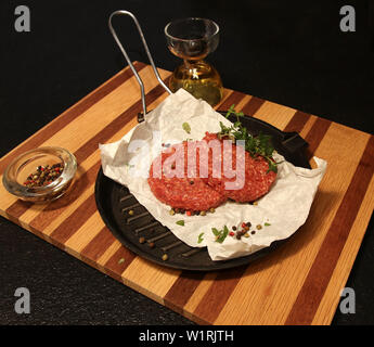 Two Beef Burgers on a skillet on a wooden board with a Black background. Stock Photo