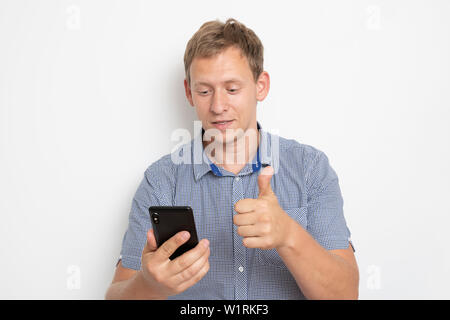 Description: Daylight Portrait of young European Caucasian isolated on white background wearing blue shirt standing in front of camera, with phone in Stock Photo