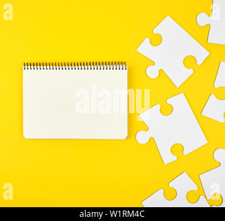 open notebook on a yellow background, next to large white blank puzzles, top view Stock Photo