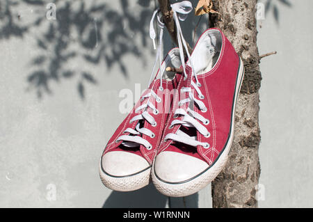 Pair of worn out vintage red old canvas sneakers hanging on their laced ties Stock Photo