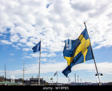 The Swedish flag of blue and gold flies along side a water way in downtown Stockholm on a beautiful sunny spring day. Stock Photo