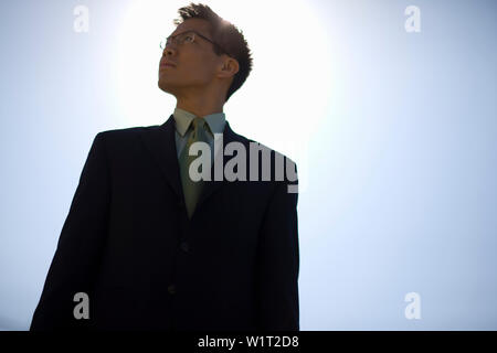 Confident young businessman standing against a clear blue sky. Stock Photo