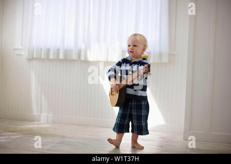 Toddler playing with a wooden banjo. Stock Photo