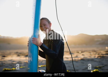 Young woman at the beach wearing a wetsuit and carrying a surfboard Stock Photo