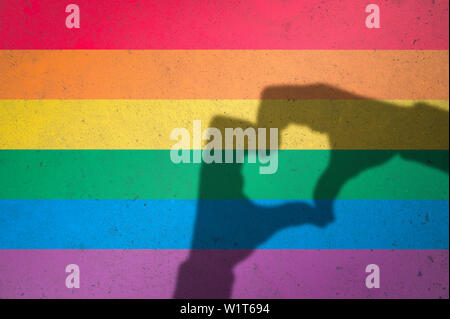 Hands making love heart shadow symbol of tolerance on gay pride rainbow colors painted on textured concrete wall background Stock Photo