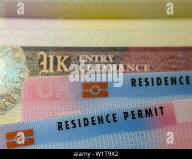 UK BRP (Biometrical Residence Permit) cards for Tier 2 work visa placed on top of UK Entry Clearance vignette sticker in the passport. Stock Photo