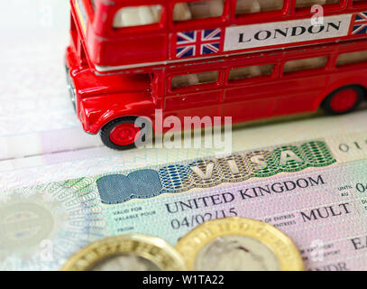 UK visa sticker in a passport surrounded by pound coins and double-decker bus model. Concept for travel and holiday. Stock Photo