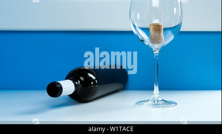 Empty wine glass on a white table next to an empty dark glass wine bottle. Cork inside Stock Photo