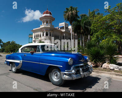 1950's American car drives past the Palacio de Valle, now a restaurant, on the Punta Gorda, Cienfuegos, Cuba Stock Photo