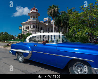 1950's American car drives past the Palacio de Valle, now a restaurant, on the Punta Gorda, Cienfuegos, Cuba Stock Photo