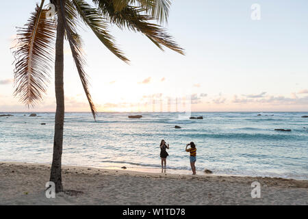 female tourists, women, taking pictures on the beach at sunset, palm tree, lonely coast road from La Boca to Playa Ancon, with beautiful small sandy b Stock Photo