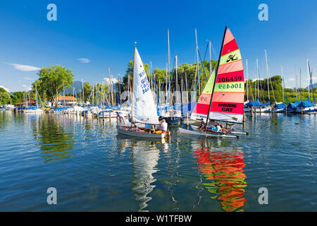 Sailors in the Port field on the Chiemsee Wieser Bay; two sailing boats are reflected in the clear water; framed by blue skies and green trees Stock Photo