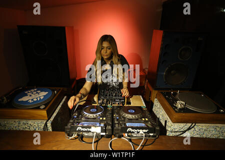 Blonde woman DJ playing and mixing vinyls in dark music club in the night. Stock Photo