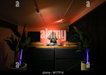 Blonde woman DJ playing and mixing vinyls in dark music club in the night. Stock Photo