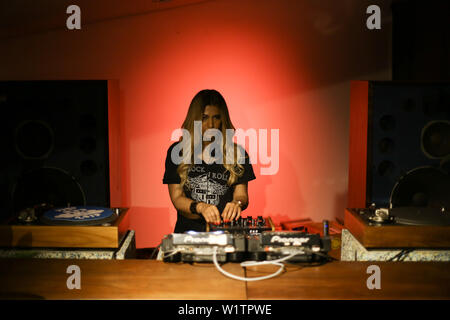 Blonde woman DJ playing and mixing vinyls in dark music club in the night. Stock Photo