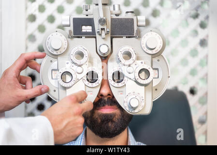 Optometrist doing sight testing for male patient In clinic. Male ophthalmologist examining patient man with optometrist trial frame .  Stock Photo