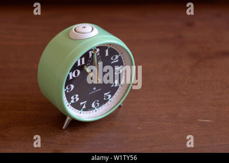 An old mechanical alarm clock on a wooden table, showing eleven o'clock. Stock Photo