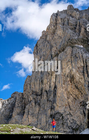 Woman hiking in front of rock face, Passo della Cavalla, Val Maira, Cottian Alps, Piedmont, Italy Stock Photo