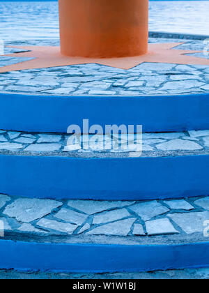 blue stone steps leading to an orange mast by the sea Stock Photo