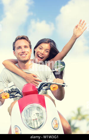 Happy young couple enjoying scooter ride against sky. Cheerful woman with arm raised screaming while man driving vehicle. Carefree male and female are enjoying their summer vacation. Stock Photo