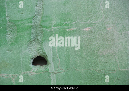 Pretty deteriorated wall that has a hole in its surface and is painted light green Stock Photo