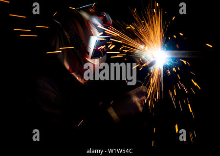 male welder in a mask performing metal welding. photo in dark colors. sparks flying.