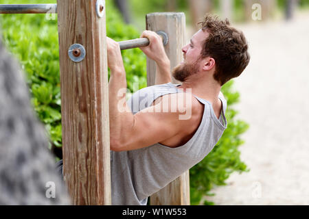 Pull-up strength training exercise - fitness man working out his arm muscles on outdoor beach gym doing chin-ups / pull-ups as part of a crossfit workout routine. Stock Photo