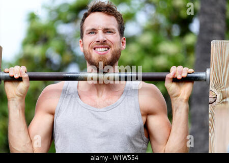 Crossfit fitness man exercising chin-ups workout. Young male adult trainer athlete portrait closeup with hands holding on monkey bars at outdoor gym doing a chin-up strength training muscle exercise. Stock Photo