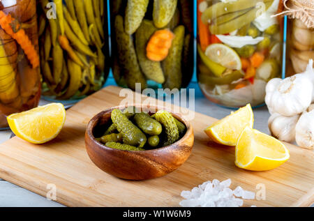 Bowl of pickled cucumbers and jars of pickled vegetables on wooden Stock Photo