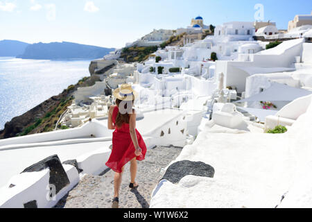 Santorini travel tourist woman on vacation in Oia walking on stairs. Person in red dress visiting the famous white village with the mediterranean sea and blue domes. Europe summer destination.